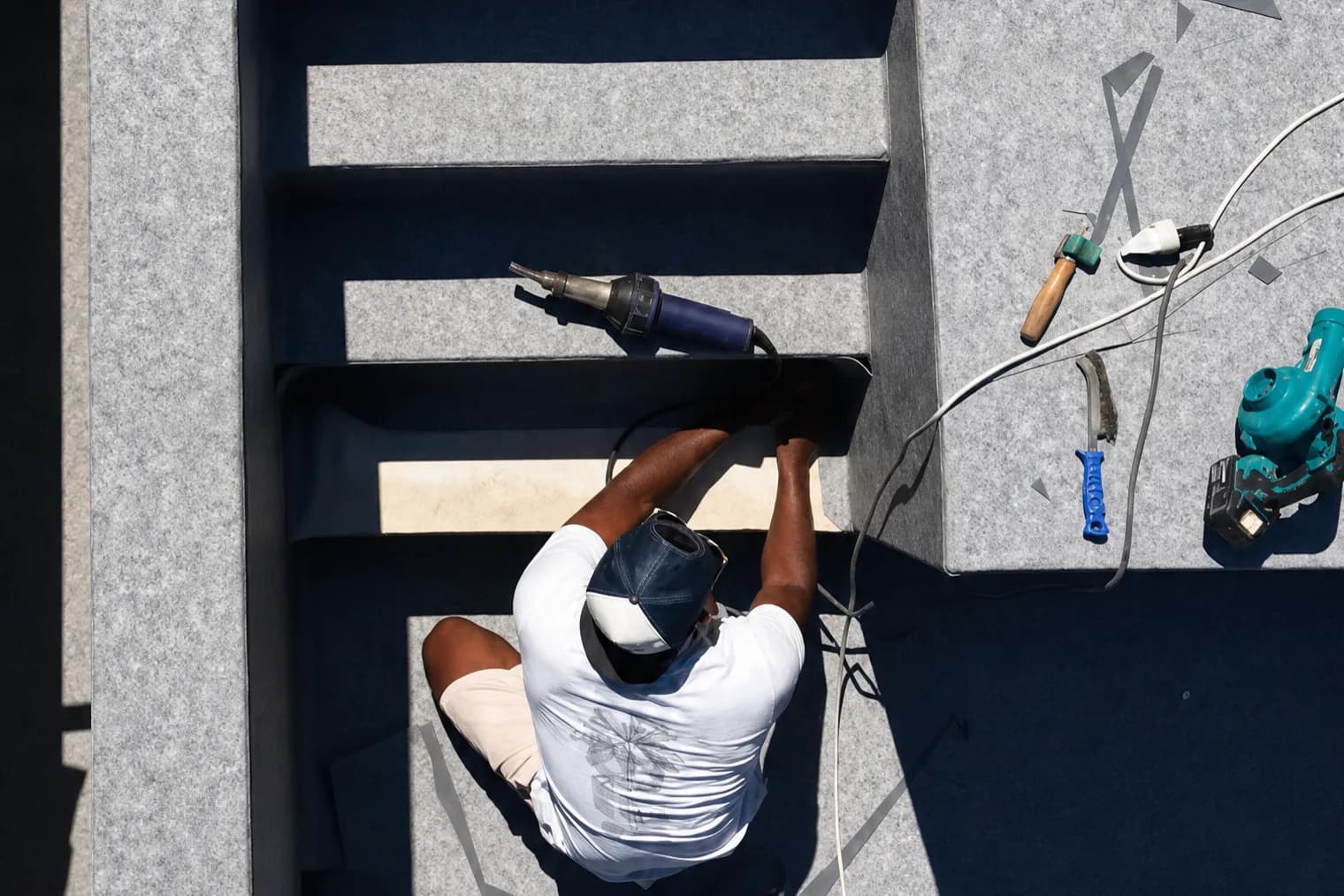 Vue de haut de Bryan Elbaz soudant au Leister les marches d'un escalier de piscine en membrane grise